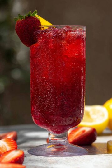 A refreshing hibiscus strawberry lemonade served over ice in a tall glass, garnished with fresh strawberries and lemon slices.