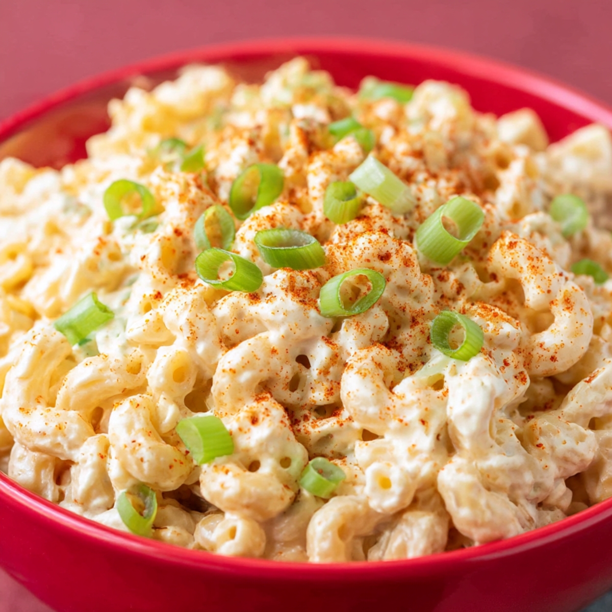 A bowl of creamy deviled egg pasta salad, topped with chopped green onions and a sprinkle of paprika, showcasing the smooth, tangy dressing and pasta in a vibrant, appetizing dish. Perfect for gatherings or potlucks.