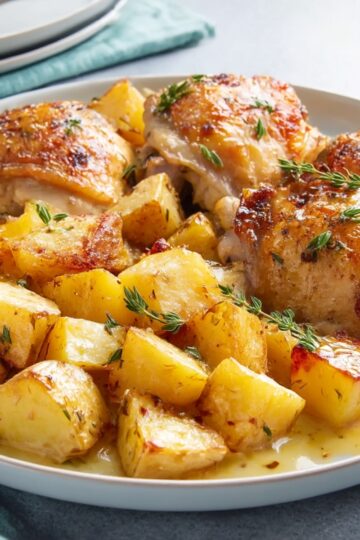 Golden roasted chicken thighs served with perfectly crispy potatoes, seasoned with thyme for a flavorful, comforting Chicken and Potatoes meal.