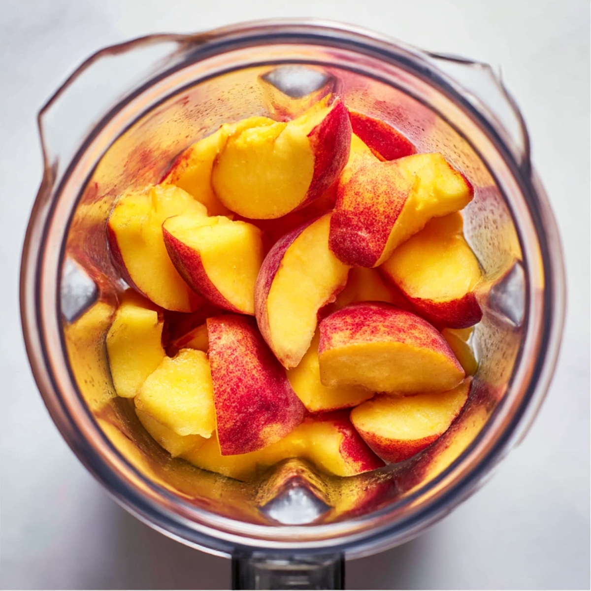 A top-down view of fresh peach slices inside a blender, ready to be blended into a refreshing homemade peach juice.