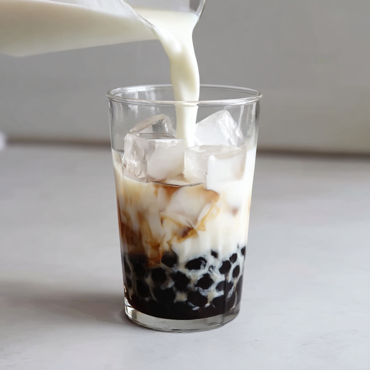 A glass of iced Matcha Bubble Tea with chewy black tapioca pearls, layered with milk and sweet matcha syrup.