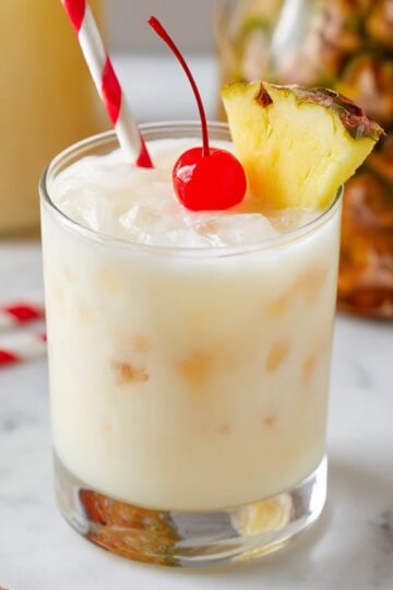 Creamy pina colada punch served over ice in a glass with pineapple wedge and cherry, tropical punch recipe