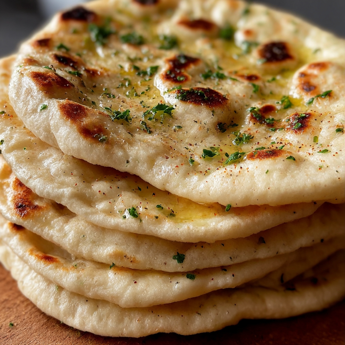 A stack of freshly baked Turkish bread, brushed with herb-infused butter and sprinkled with parsley. The bread has a golden-brown, slightly crispy surface with soft, fluffy layers inside, perfect for pairing with dips or as a side dish.