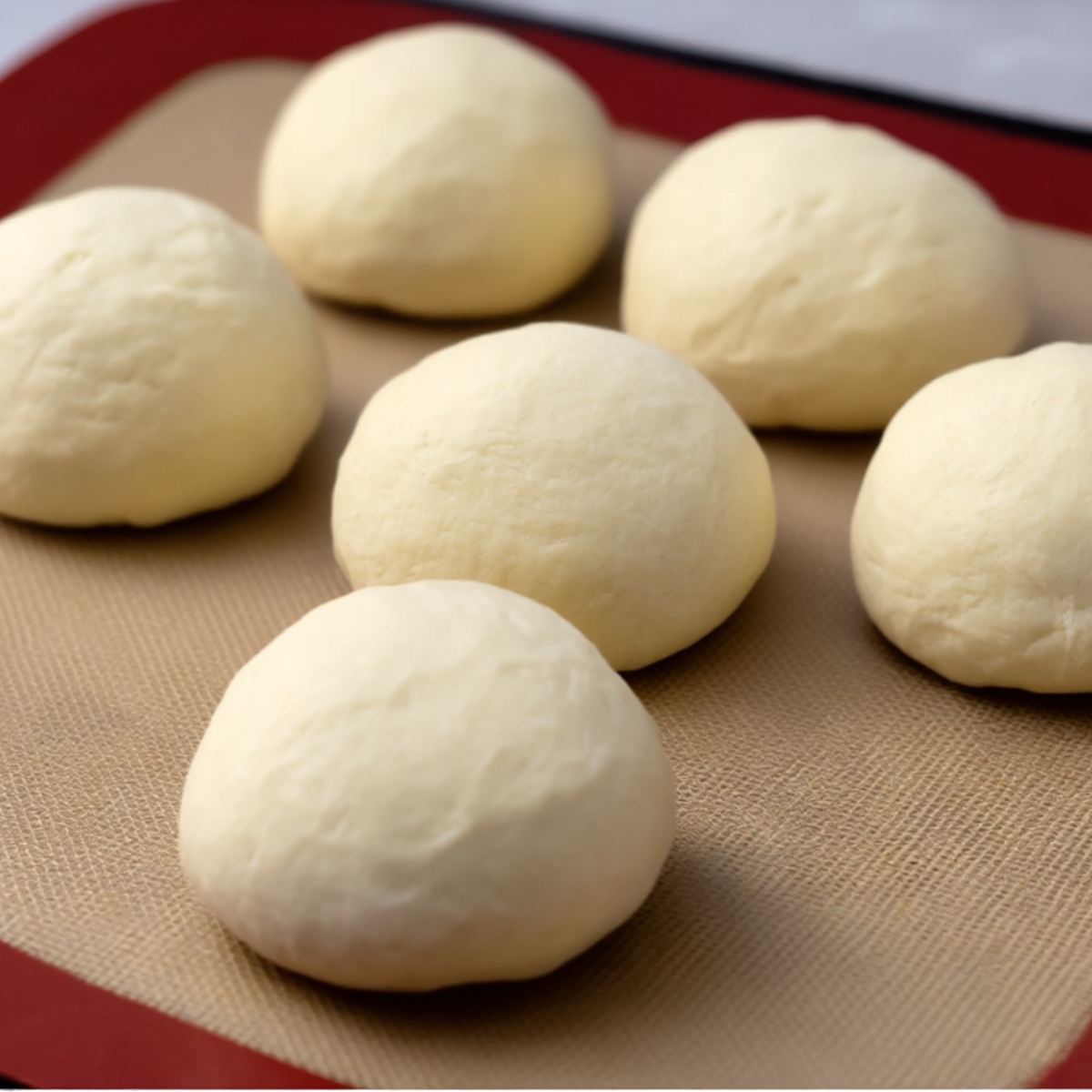 Six smooth, round dough balls placed on a silicone baking mat, ready to be baked into Turkish bread. The dough is soft and evenly shaped, demonstrating the preparation stage before baking.