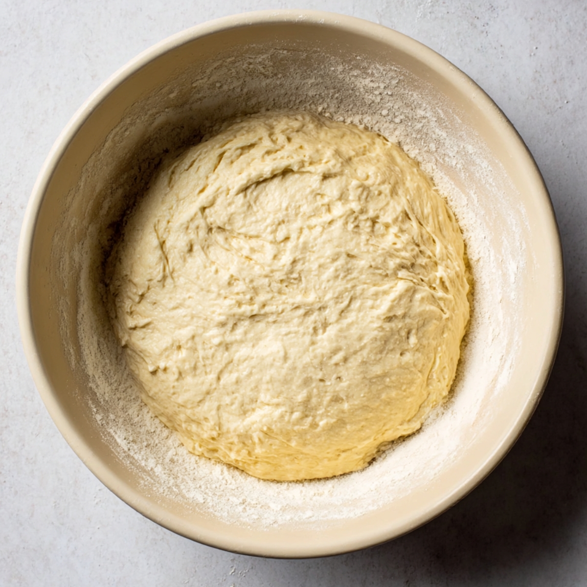 A close-up of vegan sourdough dough resting and rising in a bowl, surrounded by a light dusting of flour.