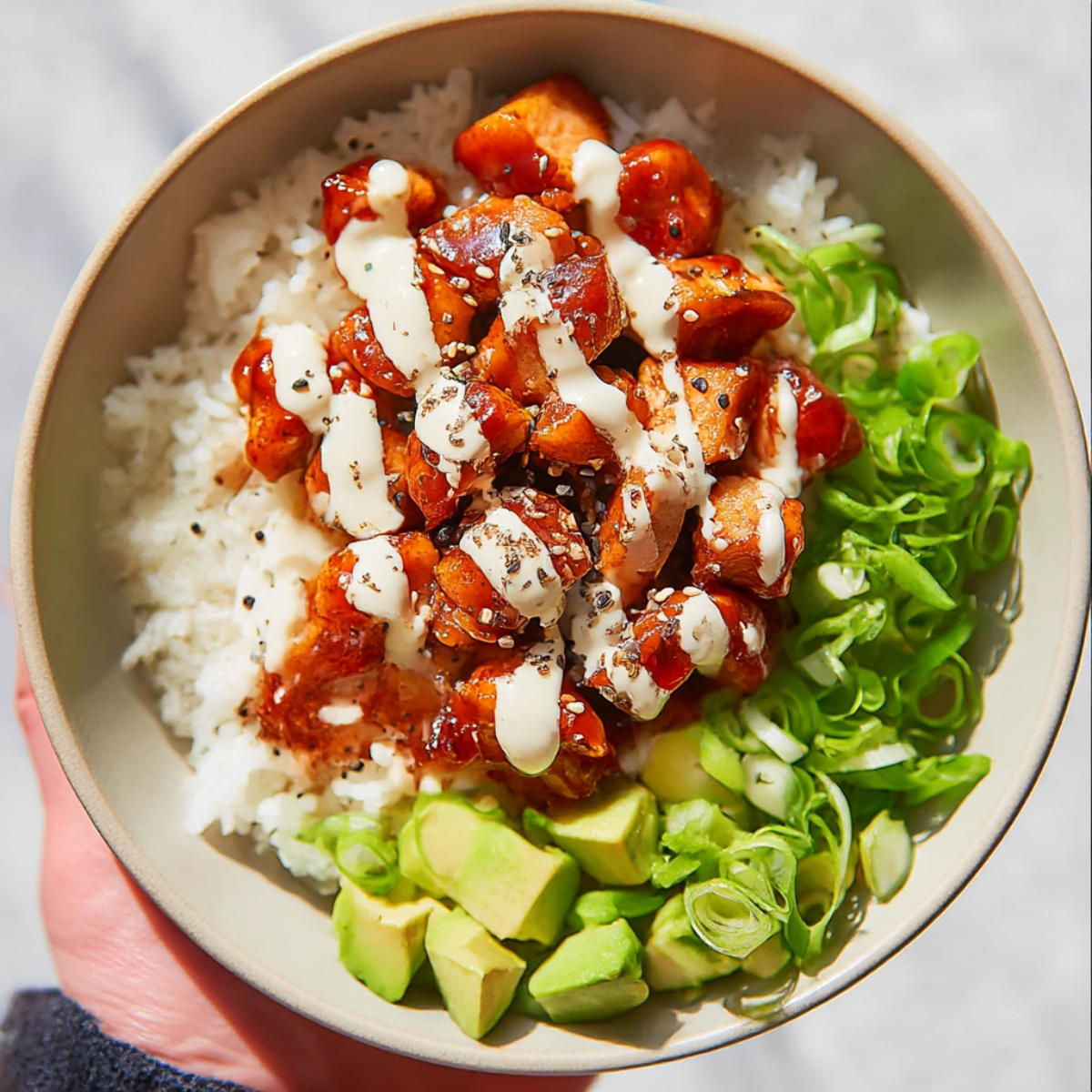 Bang bang chicken bowls with spicy glazed chicken served over white rice, topped with creamy sauce, avocado, and green onions