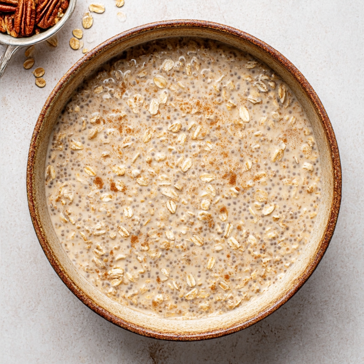 Bowl of brown sugar overnight oats soaking in milk with rolled oats, chia seeds, and cinnamon, prepared for an overnight oats breakfast recipe.