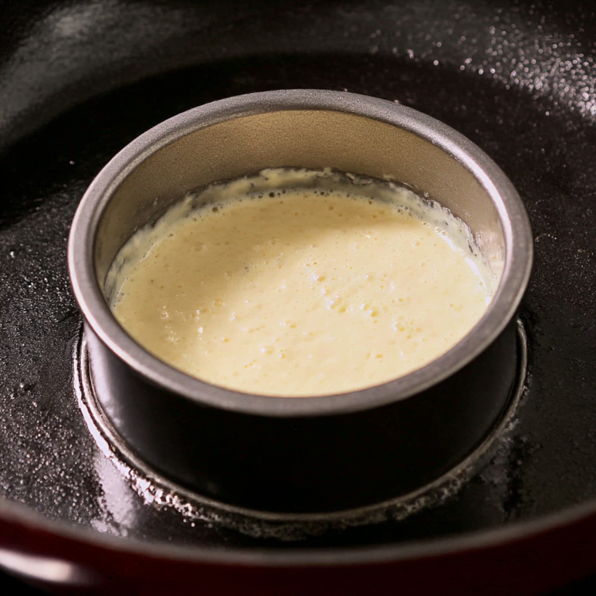 Cherry Chocolate Pancakes batter cooking in a metal ring mold on a hot skillet, creating thick and fluffy pancakes before adding cherries and chocolate.