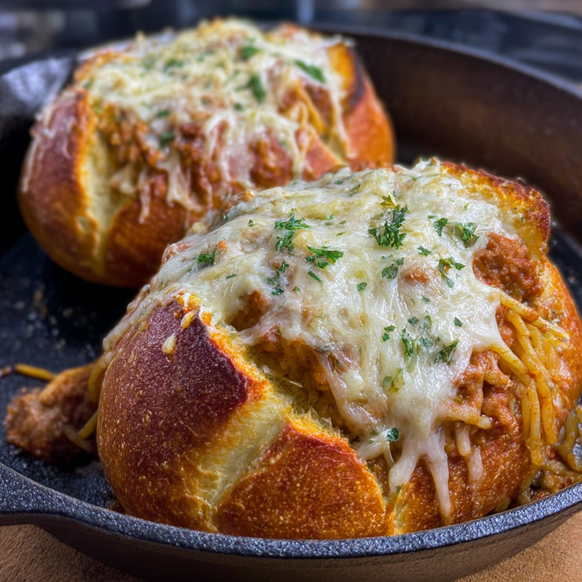Close-up of two garlic butter spaghetti bowls topped with melted cheese, parsley, and hearty meat sauce, served in a rustic cast-iron skillet.