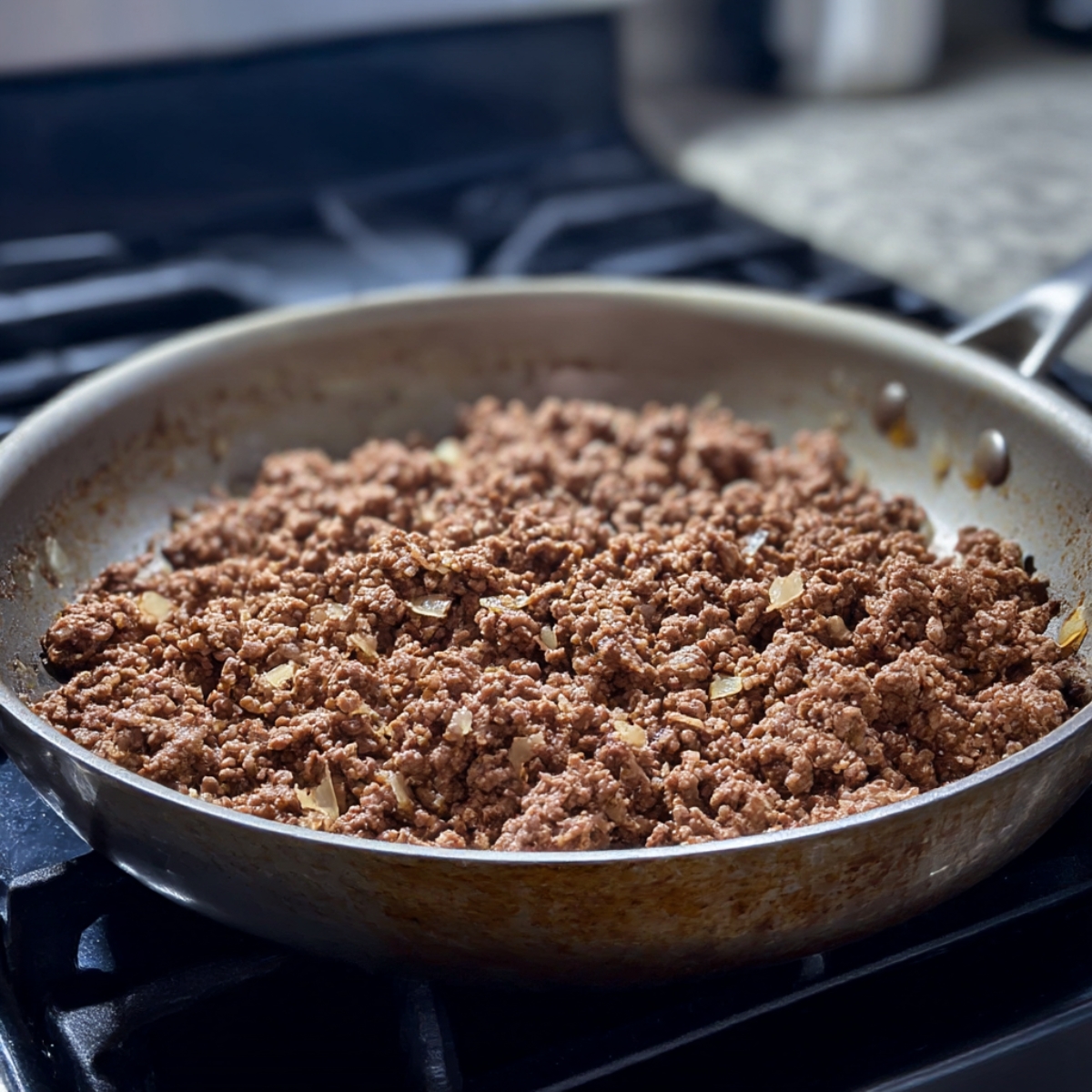 A close-up view of a skillet with browned ground beef and sautéed onions, ready to be used in a garlic butter spaghetti dish.