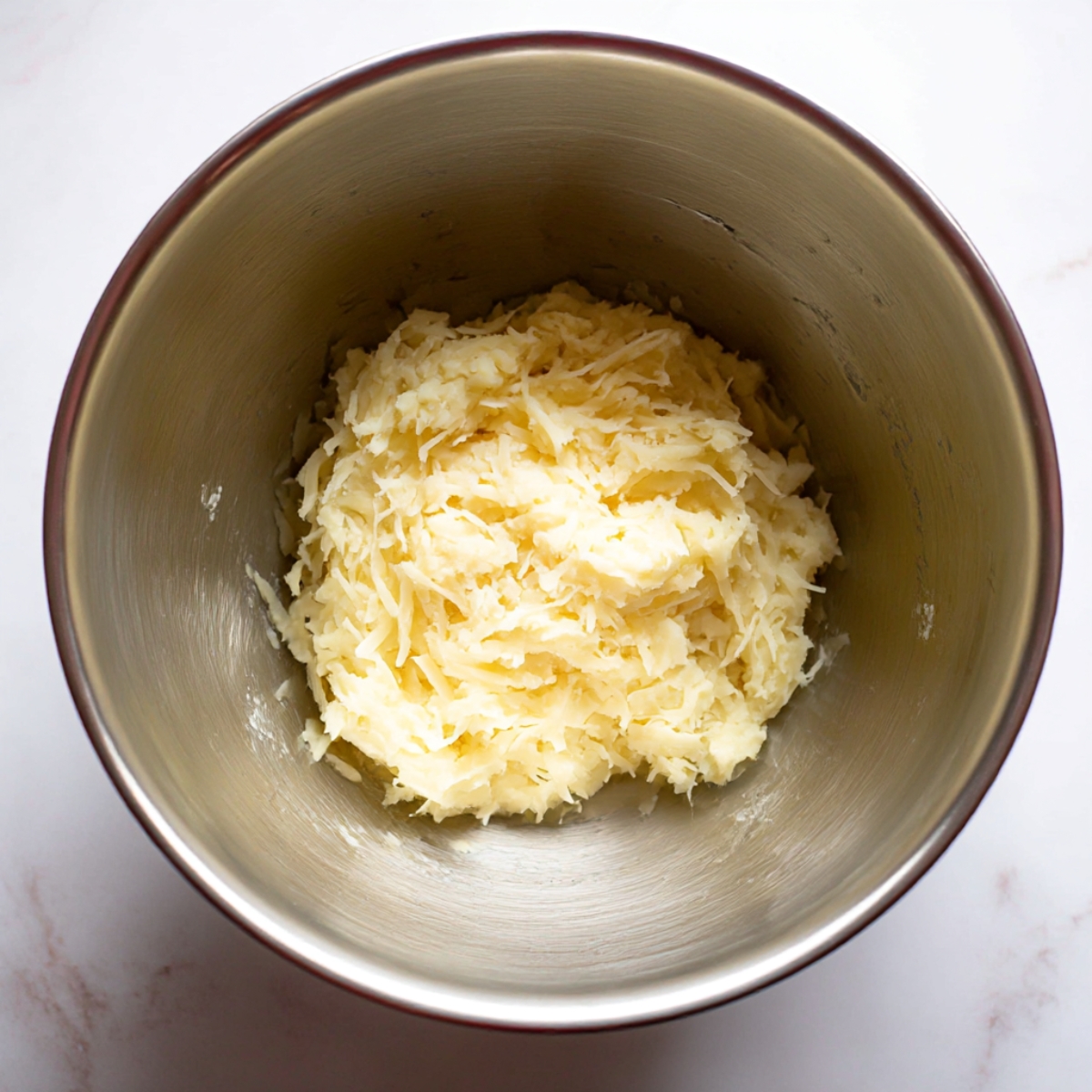 Grated potatoes in a mixing bowl prepared for traditional German Potato Pancakes.