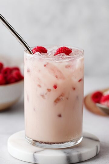 Refreshing vanilla raspberry iced drink with a creamy base, garnished with fresh raspberries and ice. Perfect for a cool, sweet summer treat.