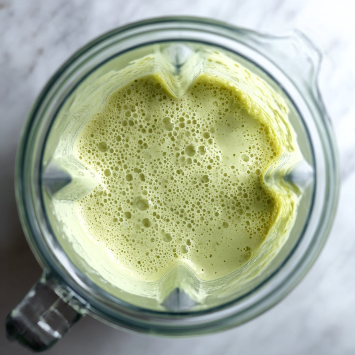 Overhead view of a blender filled with freshly blended cucumber smoothie, showing a frothy, creamy green detox drink ready to serve.