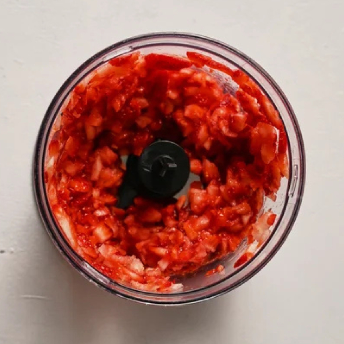 Overhead view of a blender filled with freshly chopped and blended strawberries, forming the base for a creamy Strawberry Merry Cream beverage.