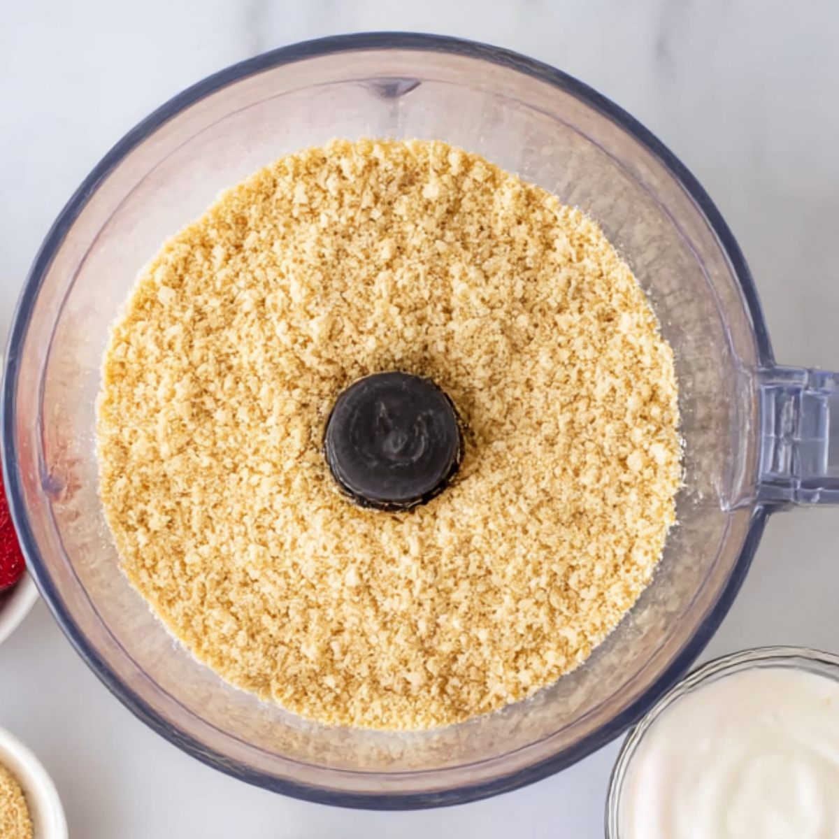 A food processor filled with finely crushed graham crackers, perfect for making the crust base for strawberry shortcake truffles. A key ingredient in creating the dessert's texture.