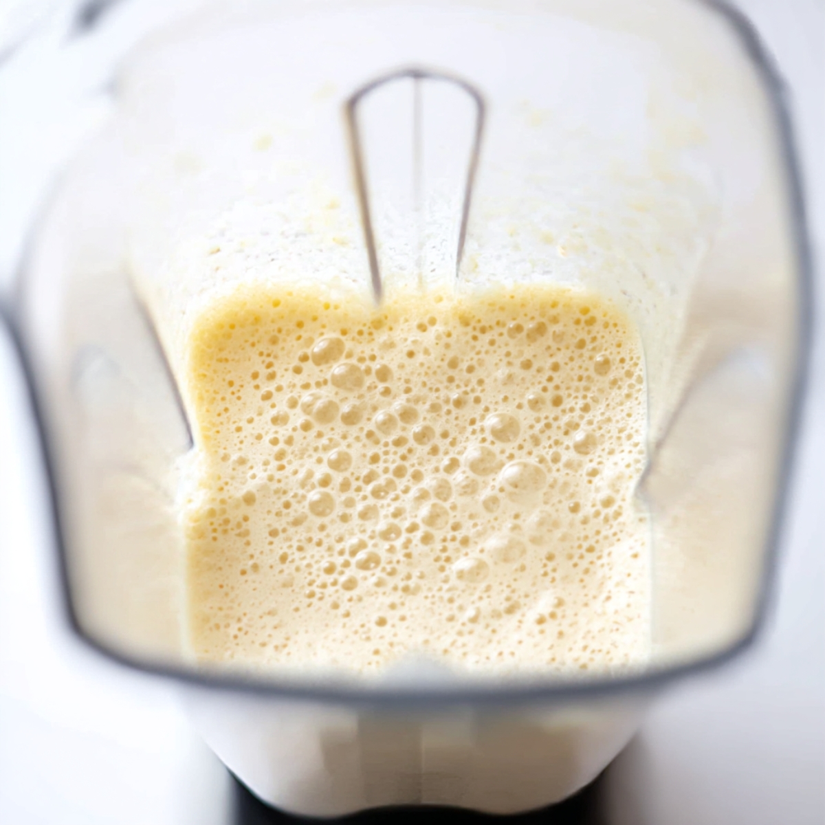 A close-up view of a blender with smooth, frothy ingredients for banana overnight oats, ready to be poured over the oats.
