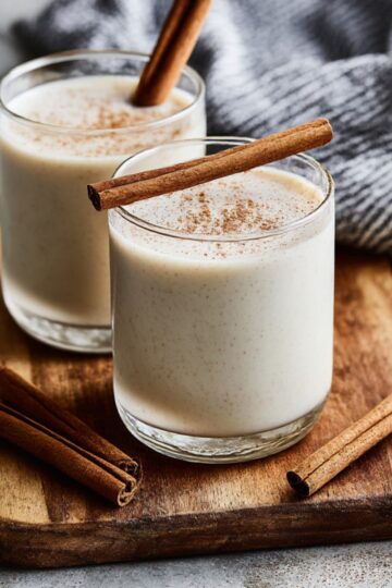 Tall glass of creamy horchata with ice, sprinkled with cinnamon on top, served on a light background with a straw, showcasing a refreshing traditional Mexican horchata recipe.
