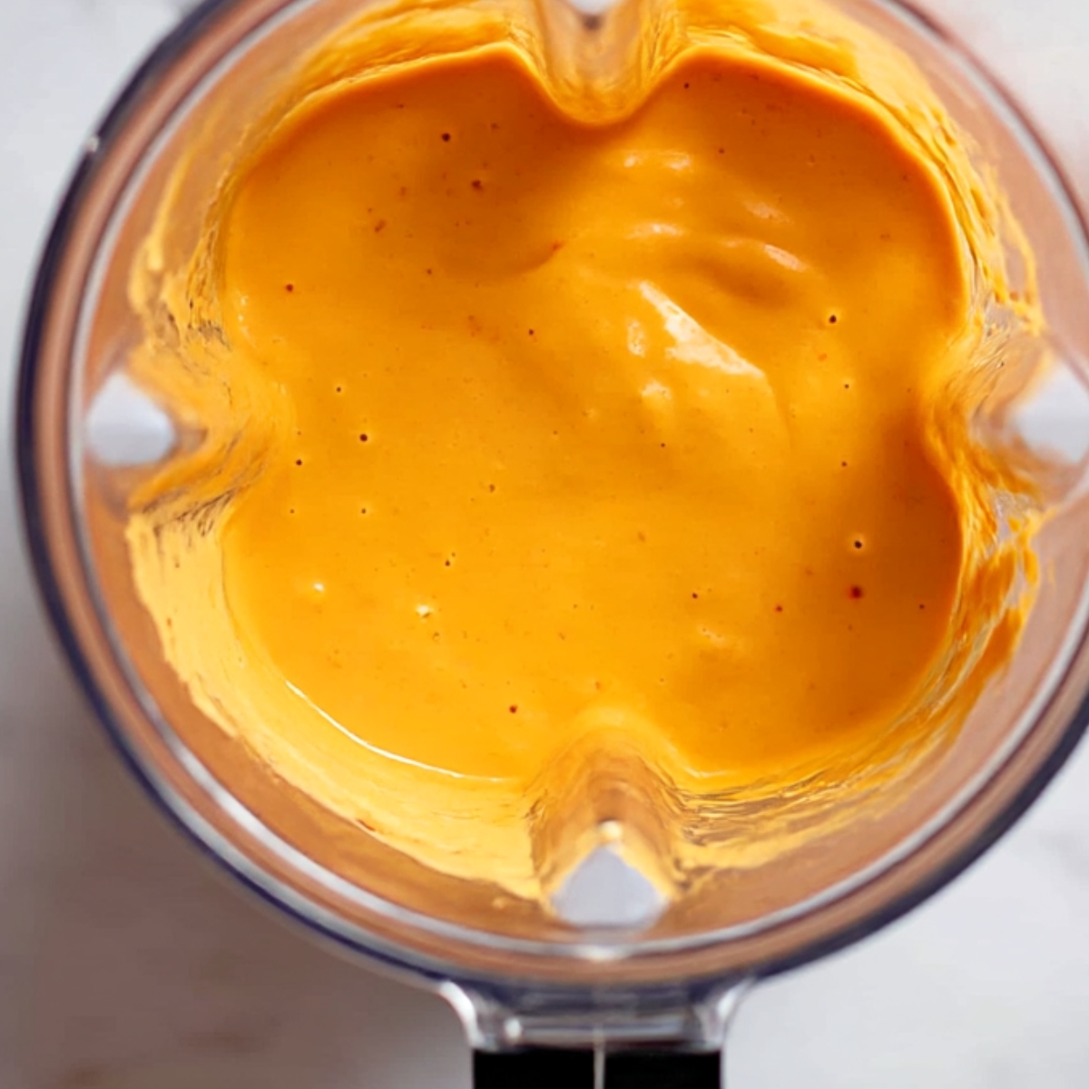 Overhead view of a blender filled with fully blended, creamy mango smoothie, showing a smooth and vibrant tropical mango drink ready to serve.