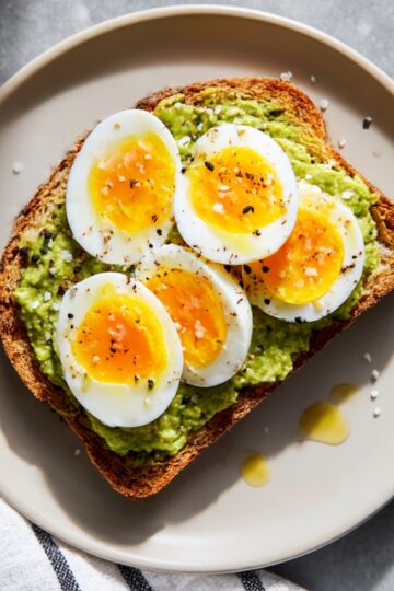 Slice of toasted bread topped with mashed avocado and perfectly sliced hard-boiled eggs, sprinkled with salt, pepper, and seeds, ready for a super quick avocado breakfast.