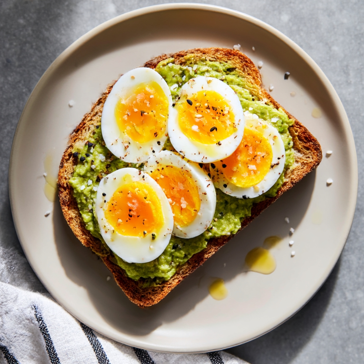 Slice of toasted bread topped with mashed avocado and perfectly sliced hard-boiled eggs, sprinkled with salt, pepper, and seeds, ready for a super quick avocado breakfast.