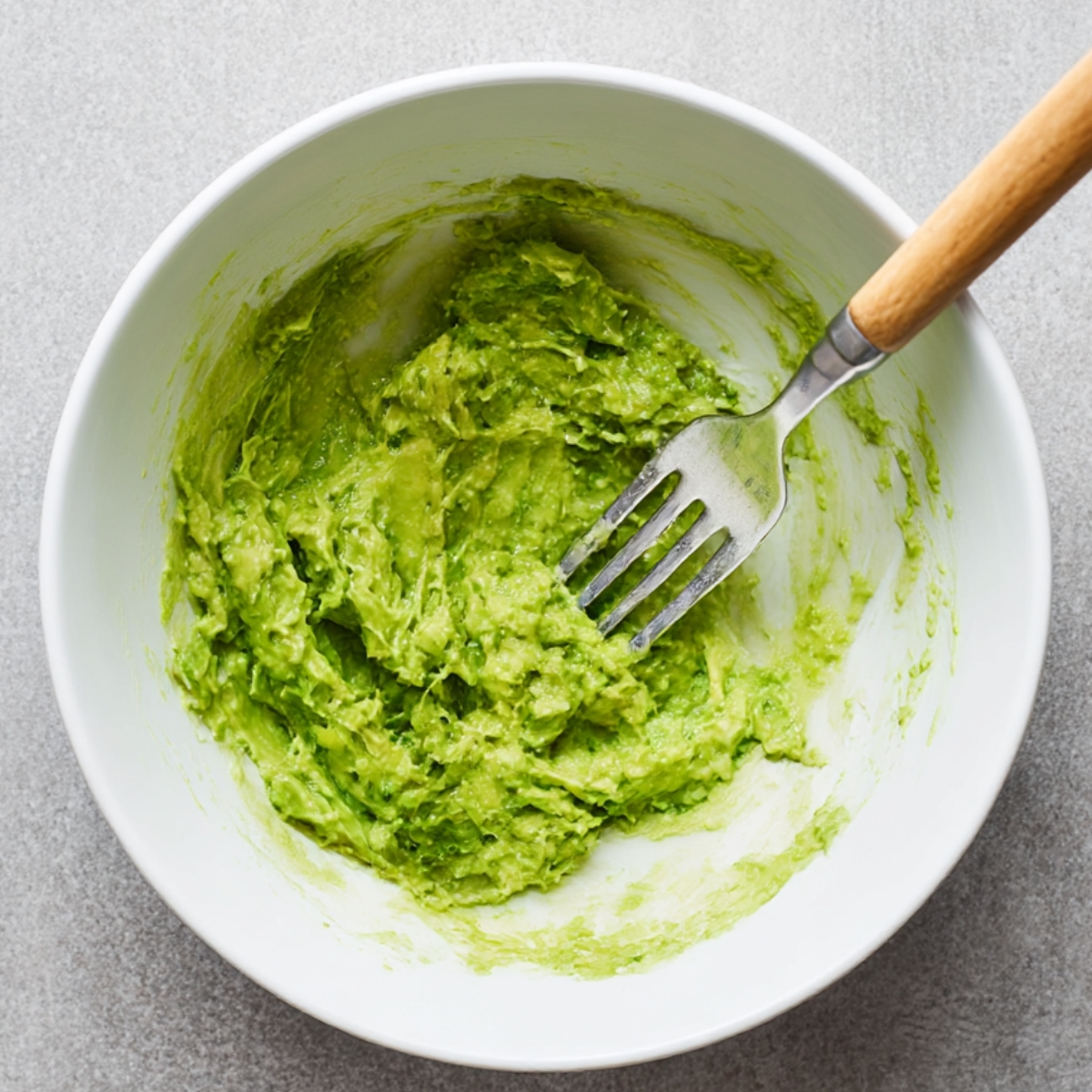 Freshly mashed avocado in a white bowl with a fork, creamy and vibrant green, perfect for making super quick avocado toast or healthy snacks.