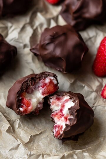 Close-up of homemade chocolate-covered strawberry yogurt clusters on parchment paper, with fresh strawberries and creamy yogurt inside the chocolate coating. Perfect easy no-bake dessert or snack.