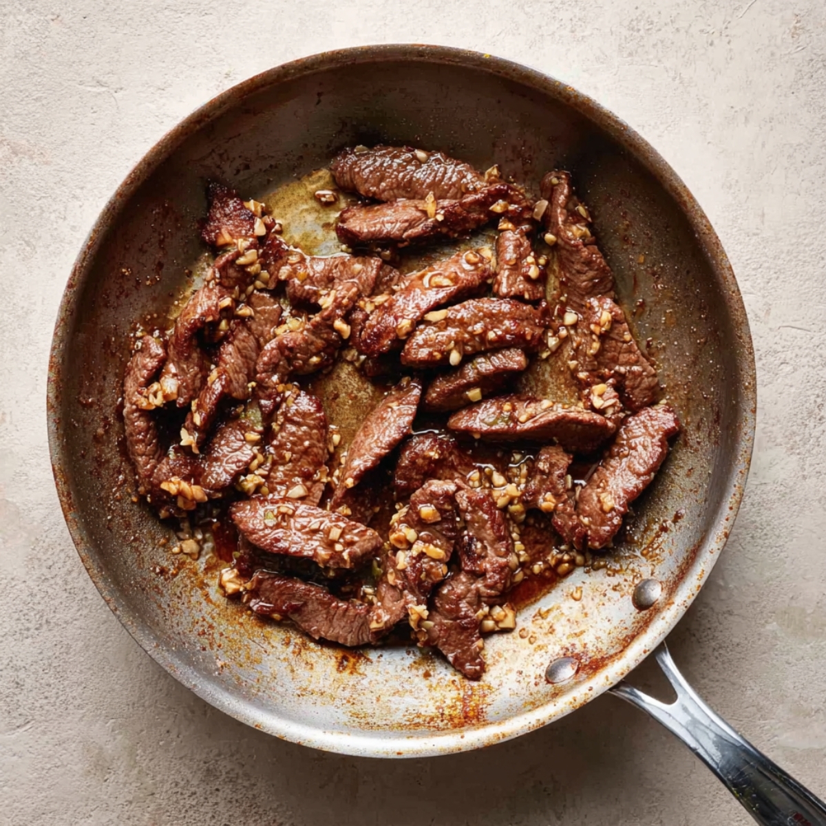 Sliced beef cooked in a savory garlic sauce in a skillet, glistening with sauce and small bits of minced garlic, ready to be combined with broccoli for a classic beef and broccoli stir-fry.