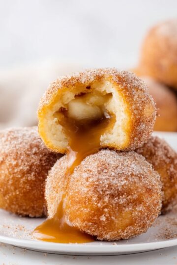 Plate of golden, cinnamon-sugar coated Caramel Apple Pie Bombs with gooey caramel filling oozing out, perfect for fall desserts and holiday treats.