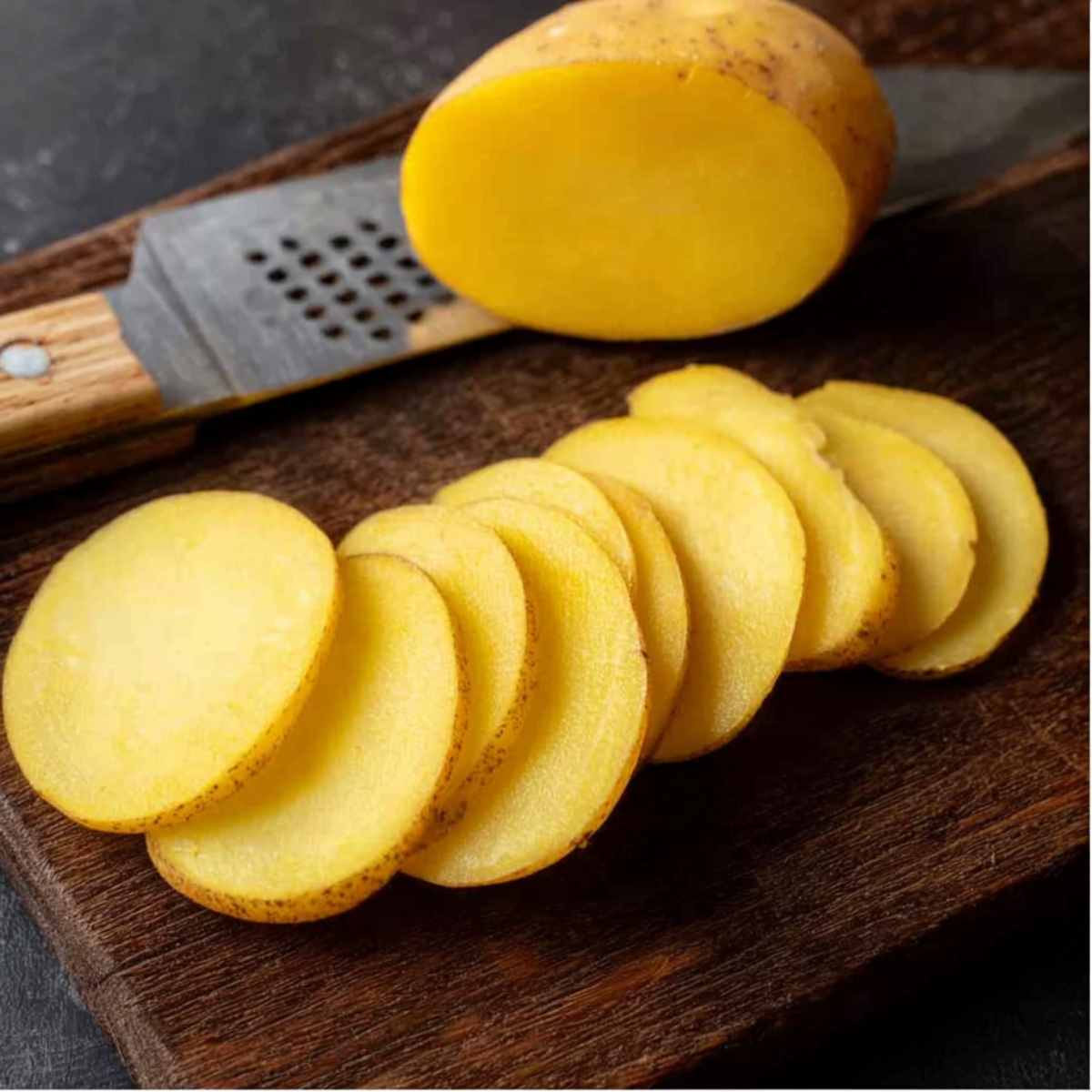 Yellow potatoes thinly sliced on a wooden cutting board with a grater in the background, ready to make a cheesy hamburger potato casserole.