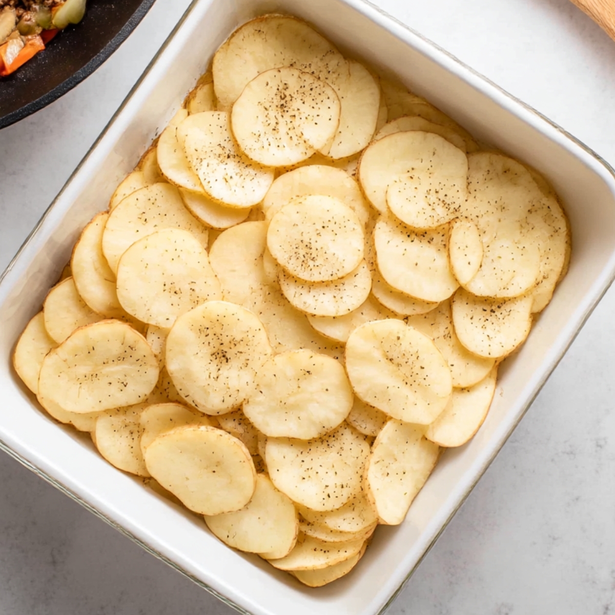 Sliced potatoes layered in baking dish for hobo casserole recipe
