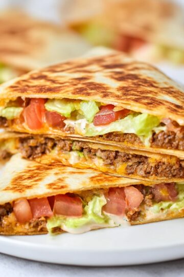 Stacked keto crunchwraps filled with seasoned ground beef, cheese, lettuce, and tomatoes on a white plate