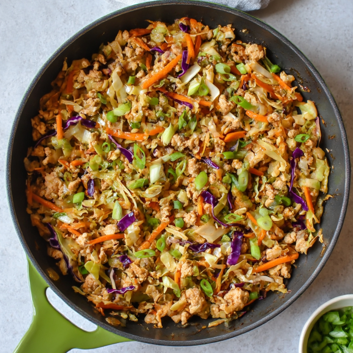A skillet filled with Egg Roll in a Bowl made with ground turkey, shredded cabbage, carrots, and green onions, cooked together in a savory sauce, ready to serve.