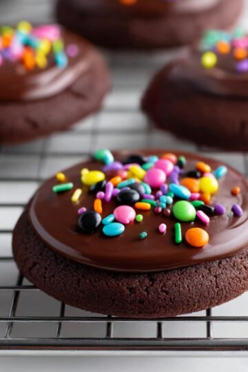 Close-up of rich, fudgy chocolate brownie cookies topped with glossy chocolate frosting and colorful cosmic sprinkles, cooling on a wire rack – perfect fudgy cosmic brownie recipe.