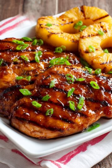 Juicy grilled Huli Huli chicken glazed with a sweet and savory Hawaiian BBQ sauce, served with char-grilled pineapple rings and garnished with fresh green onions.