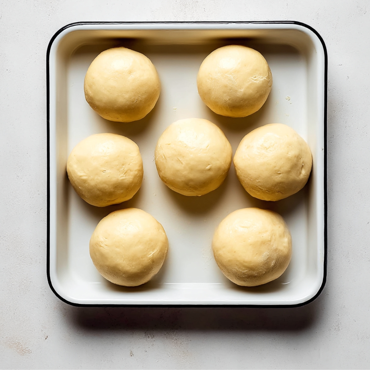 Seven smooth balls of puff pastry dough arranged in a baking tray, prepared for rolling and layering in a homemade Napoleon Cake dessert.