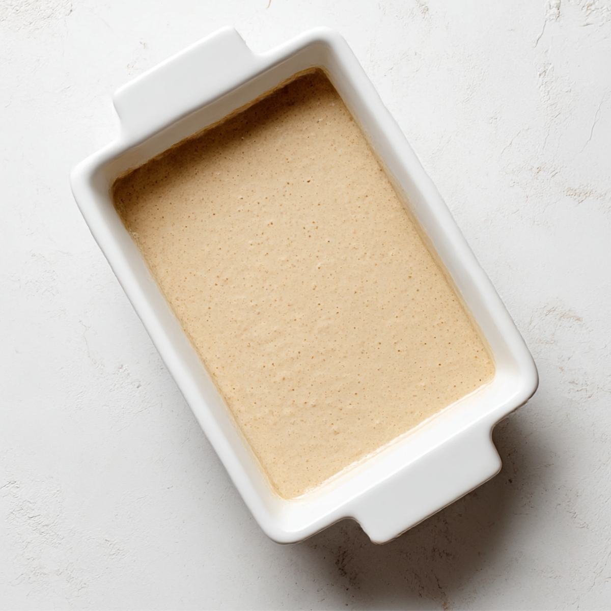 Smooth protein pancake bowl batter in a white rectangular baking dish, ready to bake, on a light textured surface, perfect for a healthy, high-protein breakfast.