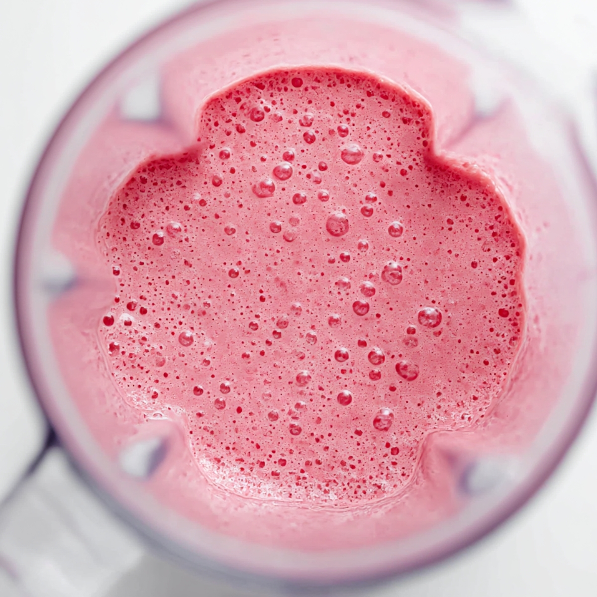 Top-down view of a vibrant pink raspberry chia pudding smoothie in a blender, with a frothy, bubbly texture, ready to pour into a serving glass.