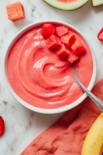 Creamy strawberry watermelon smoothie served in a bowl, topped with fresh watermelon cubes, surrounded by strawberries, banana, and watermelon slices for a vibrant summer treat.