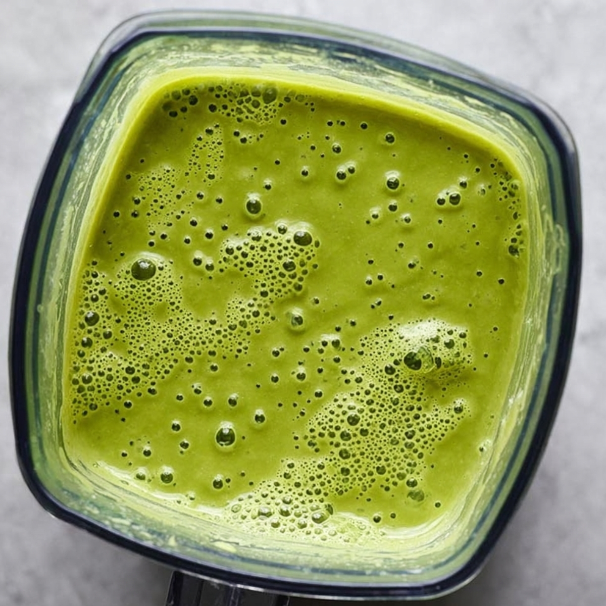 Top view of freshly blended creamy asparagus soup in a blender, showing vibrant green color and frothy texture, ready to be poured and served as a healthy meal.