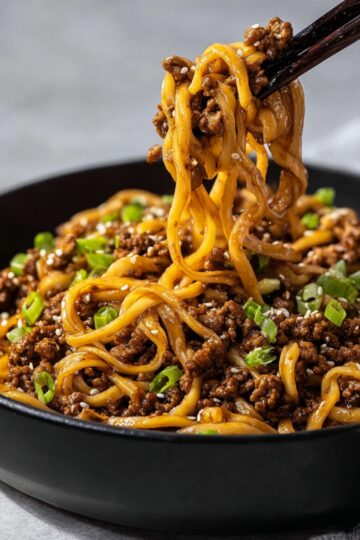 Bowl of Mongolian ground beef noodles garnished with chopped green onions and sesame seeds, showing tender noodles coated in savory, rich sauce, perfect for an easy weeknight dinner.