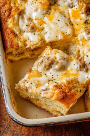 A close-up of a baked biscuits and gravy breakfast casserole in a rectangular dish, featuring fluffy golden biscuits topped with creamy sausage gravy and melted cheese, ready to serve.