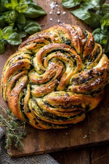 Freshly baked swirled garlic herb bread with golden brown crust, flaky layers, and vibrant green herb filling on a wooden board, garnished with fresh basil and coarse sea salt.