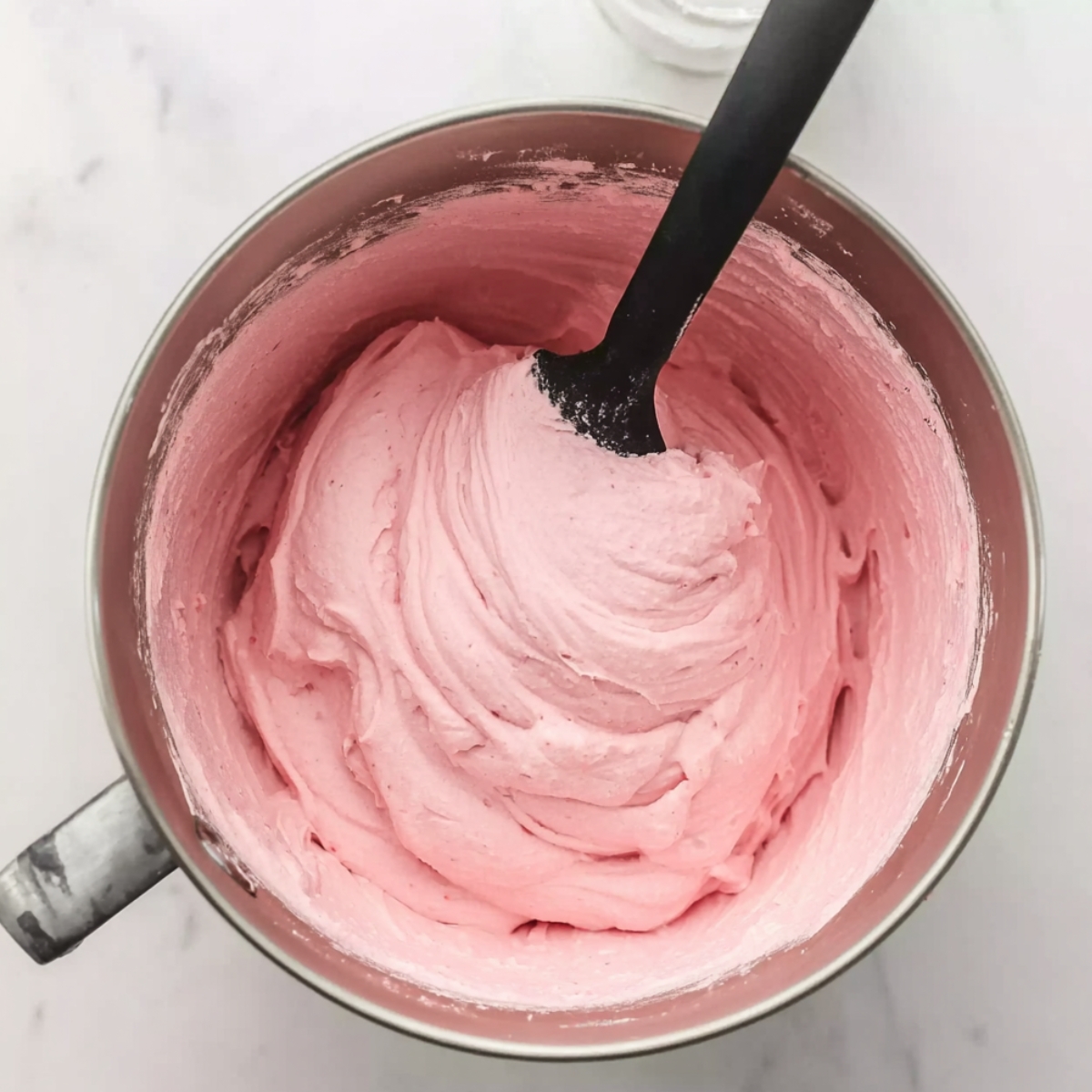 Top view of a mixing bowl filled with smooth, pink raspberry mousse being stirred with a spatula, showing creamy texture for a homemade dessert.