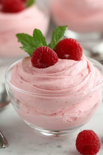 Delicious pink raspberry mousse in a glass bowl, garnished with fresh raspberries and mint leaves, perfect for a light and creamy dessert.