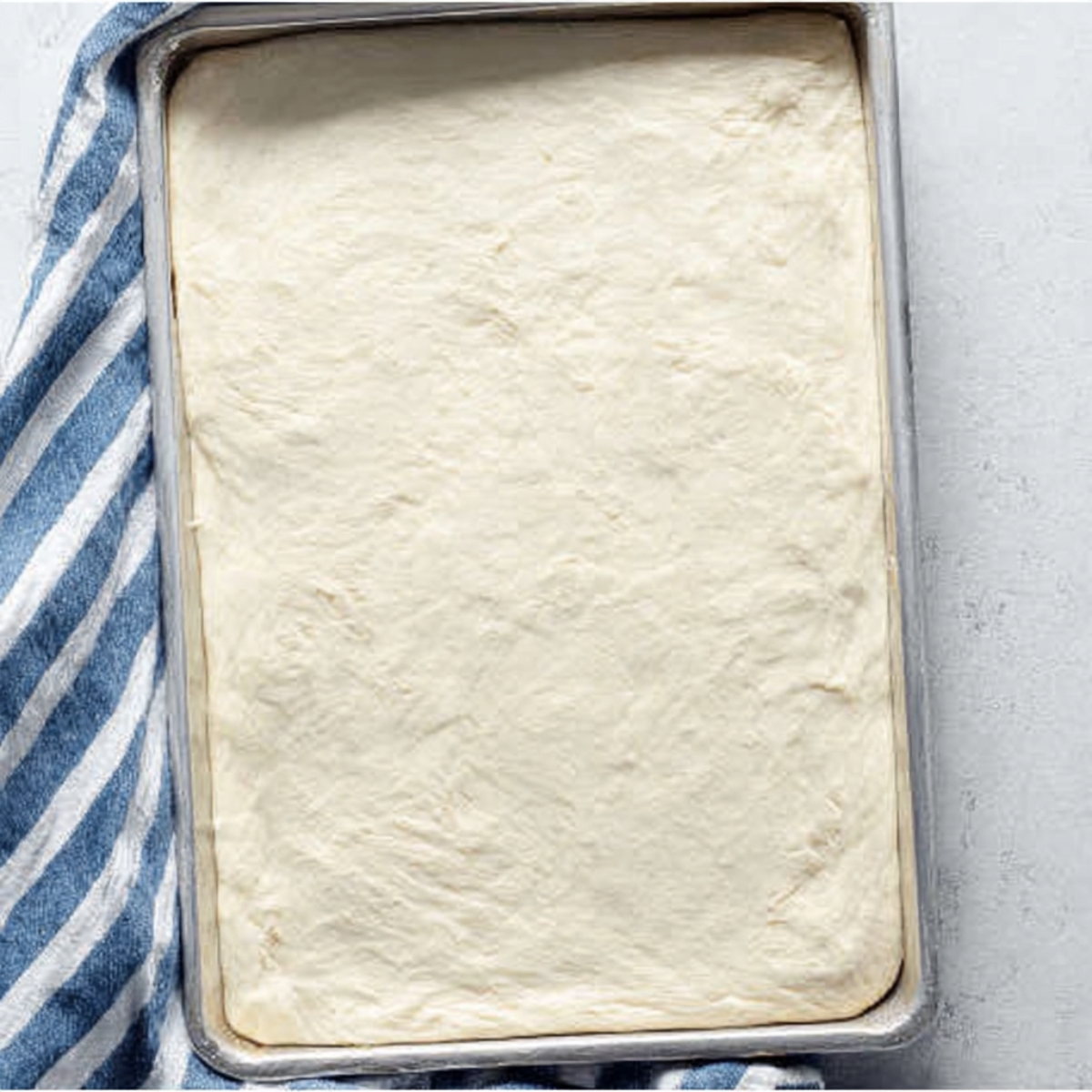 Raw pizza dough pressed into a baking sheet, ready for cheese topping, to make homemade Copycat Pizza Hut style cheese sticks.