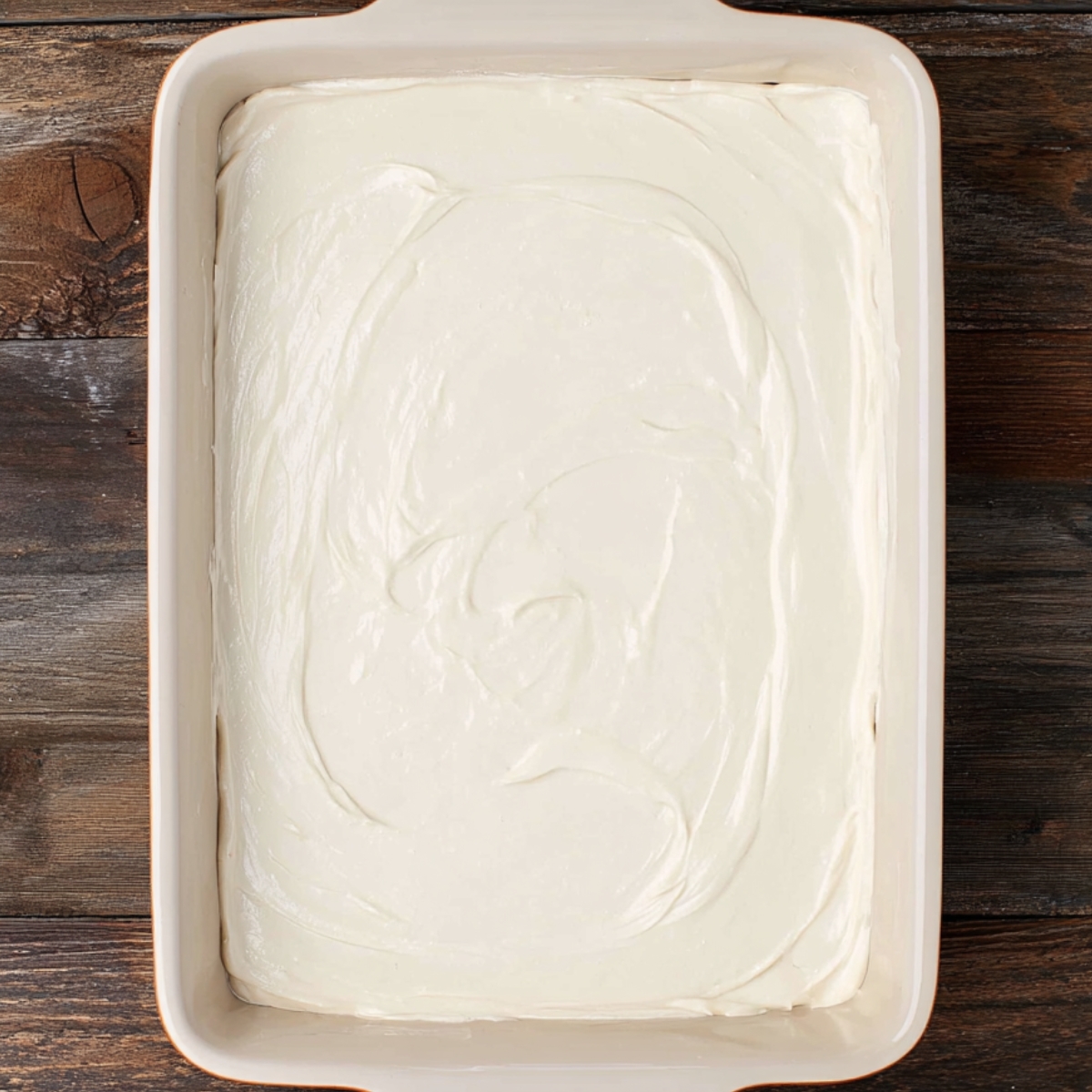 A baking dish filled with a smooth, creamy layer spread over a cookie crumb base, partway through making a Vanilla Lush Pie.